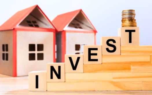 Image Of Miniature House Models Surrounded By Wooden Cubes With The Inscription 'Invest,' Representing The Concept Of Real Estate Investment.