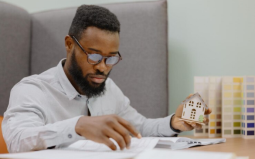 An African American male architect-engineer or designer is seen working in an office on plans for a residential building.